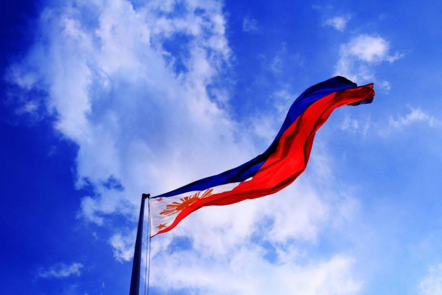 The flag of the Philippines billows in front of a clouded blue sky