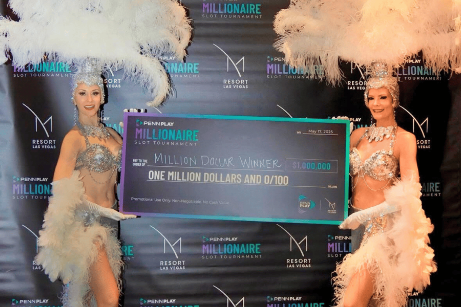 Kansas guest walks away with $1 million at 2025 PENN Play tournament. Two showgirls in sparkling costumes and feathered headdresses hold a giant ceremonial check for $1,000,000 at the 2025 PENN Play Millionaire Slot Tournament at M Resort Spa Casino. The backdrop features branding for PENN Play and M Resort Las Vegas.