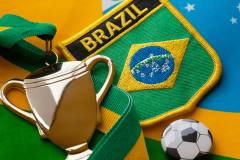 Senator Girão urges sports betting ban in Brazil amid warning of soccer threat. Close-up image of a gold trophy medal with a green and yellow ribbon, placed alongside a Brazil football team badge, the Brazilian flag, and a small soccer ball pin.