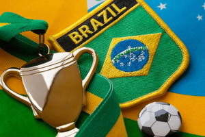 Senator Girão urges sports betting ban in Brazil amid warning of soccer threat. Close-up image of a gold trophy medal with a green and yellow ribbon, placed alongside a Brazil football team badge, the Brazilian flag, and a small soccer ball pin.