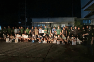  Vietnam’s Ministry of Public Security. A large group of arrested suspects, many wearing masks, sit or kneel in front of uniformed Vietnamese and Lao police officers during a nighttime transfer operation.