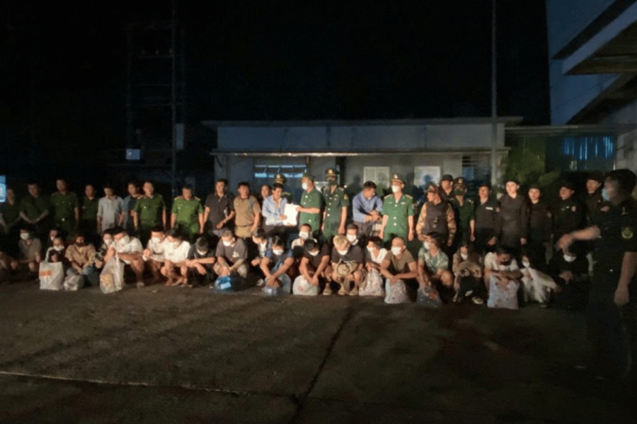 Credit: Vietnam’s Ministry of Public Security. A large group of arrested suspects, many wearing masks, sit or kneel in front of uniformed Vietnamese and Lao police officers during a nighttime transfer operation.