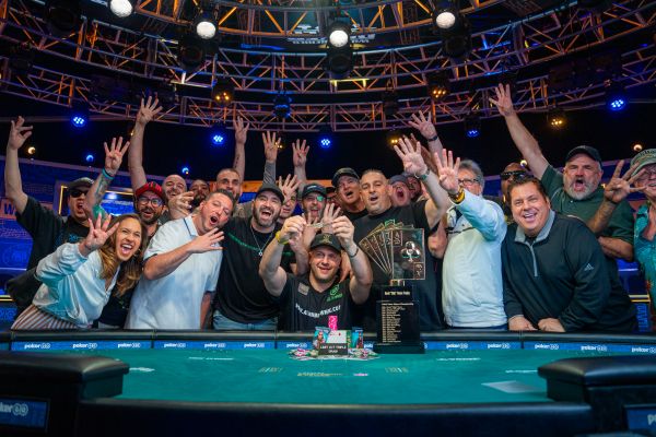 Poker table with people crowded around in the background. All celebrating with arms in the air.