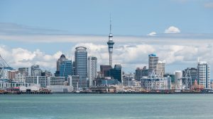 The Skyline of Auckland as seen from Devonport, located at the North Shore. Blue water in the forefornt, buildings in the background. Blue sky.