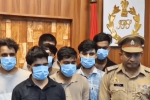 Police bust international cricket betting racket in India after fake kidnapping tip. Group of men with blue face covers standing behind police officer following arrest.