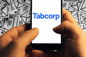 Tabcorp fined $4M for spamming VIPs with unlawful marketing messages. Person holding a smartphone displaying the Tabcorp logo, with a background of illustrated email icons representing spam or mass marketing messages.