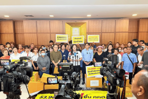 Thai citizens submit 54k-signature petition demanding referendum against casino legalization. A group of Thai citizens stand together at a press conference, holding signs and banners while submitting a petition with 53,900 signatures to the Election Commission of Thailand. Boxes of signed petitions are stacked in front of them, and several media cameras are capturing the event. Signs in Thai and English read “NO CASINO ต้องประชามติ” and “ประชามติประชาชน.”