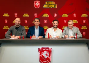 Four men sat at a table, all smiling. FC Twente football logo on the front of the table and Eurojackpot logo in the background.