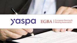 Yaspa logo next to EGBA logo on a white banner, with someone signing a piece of paper behind it.