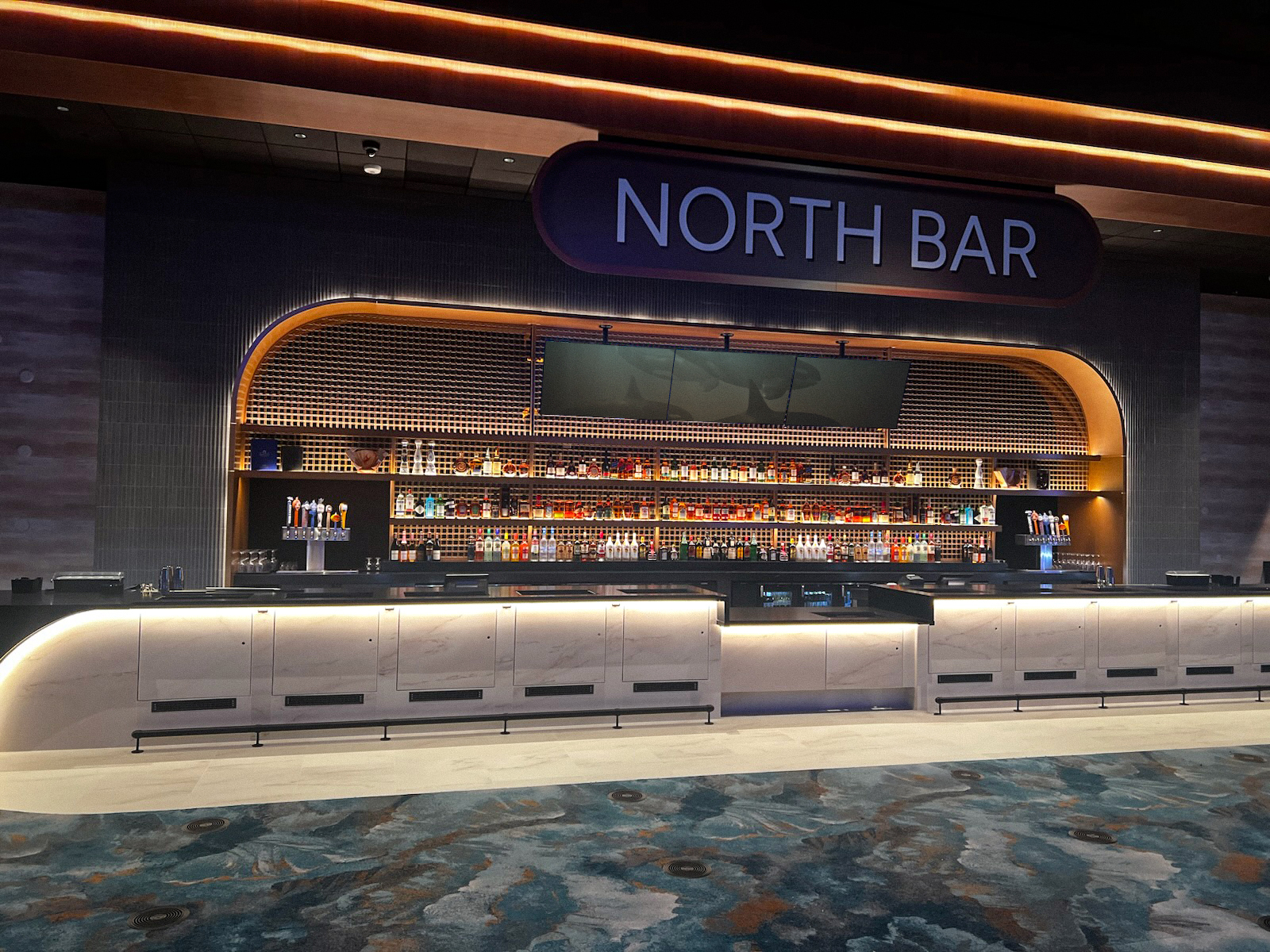 Modern bar area named “North Bar” with sleek lighting, rows of liquor bottles, multiple beer taps, and a stylish contemporary design featuring curved shelving and illuminated countertops at Tulalip Resort Casino.