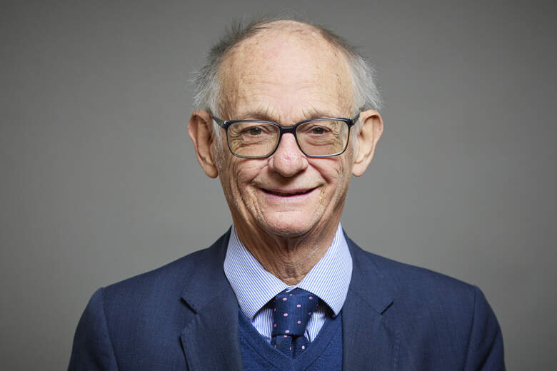 Man wearing a dark navy suit and light blue shirt stood against a plain grey background.