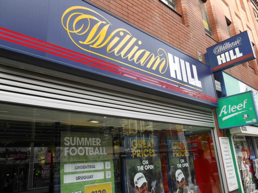 Front of a William Hill store front, can see the blue logo and grey shutters at the top.