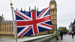 A photograph of a vibrant Union Jack flag billowing gently in the breeze, positioned prominently in front of the Houses of Parliament in London. UK APPG launches inquiry into the future of gambling regulation
