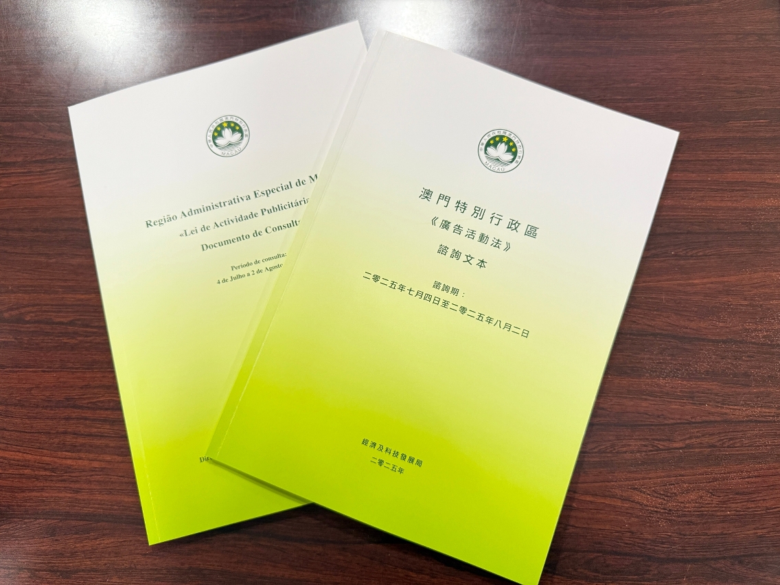 Two consultation documents from the Macau SAR Government on proposed amendments to the Advertising Activity Law, placed on a wooden table.