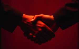 Two hands shaking on a deep red background. Former Ladbrokes CEO charged in Turkish bribery case 