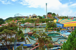 Colorful outdoor amusement park in Genting Highlands, Malaysia, featuring roller coasters, water rides, a central lake with paddle boats, and vibrant buildings under a bright blue sky. Genting Highlands casino chips theft suspect 'on the run'