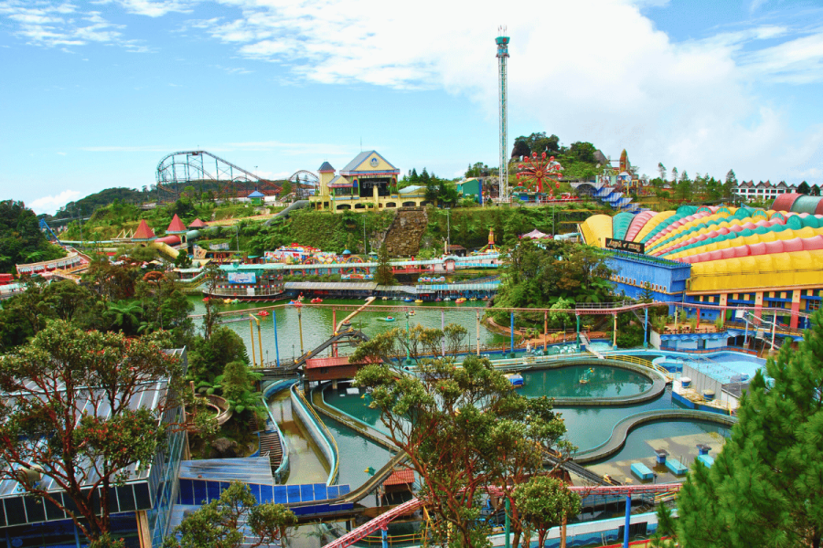 Colorful outdoor amusement park in Genting Highlands, Malaysia, featuring roller coasters, water rides, a central lake with paddle boats, and vibrant buildings under a bright blue sky. Genting Highlands casino chips theft suspect 'on the run'