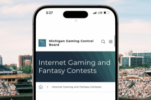 Basebol image and iPhone over it, with the Michigan Games Control website open on the phone. MGCB commands 15 illegal gambling sites to stop Michigan operations immediately
