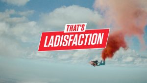 Clouds in the sky with 'That's Ladisfaction' in the center and a man skydiving below this.