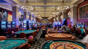 A photo of the inside of a casino with a variety of games. There are slot machines, roulette wheels, and poker tables. The walls are adorned with chandeliers and paintings. The floor is checkered. There are people playing the games. The background is dimly lit. Betting and Gaming Council strongly rejects IPPR findings on gambling tax hike