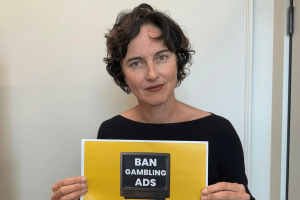 MP Kate Chaney holds up sign that says "Ban Gambling Ads." RWA criticized for gambling ties to Australian Parliament Sports Club