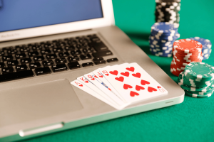Gambling Commission report explores motivations behind illegal online gambling choices. Playing cards showing a royal flush placed on a laptop keyboard with poker chips stacked beside it on a green felt table.