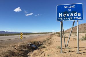Welcome to Nevada sign long southbound U.S. Route 95 entering Clark County, Nevada from San Bernardino County, California, dusty road and blue sign at the side of the road. Nevada regulator issues firm stance on sports event contracts
