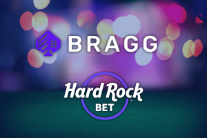 Logos of Bragg Gaming and Hard Rock Bet displayed on a colorful, blurred background with purple, blue, and pink bokeh lights. The Bragg logo and name appear at the top, while the Hard Rock Bet logo is positioned below within a purple circle. Bragg Gaming launches new titles for Hard Rock Bet Casino