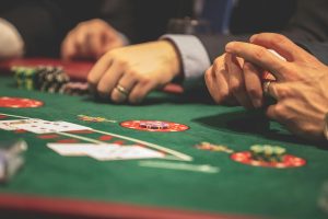 California tribes were prevented from suing card rooms because of the state's exclusive rights. Close-up of people playing poker at a casino table, with playing cards, chips and hands visible on the green felt surface.