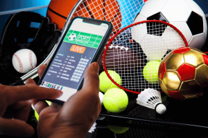 A person uses a smartphone to place a live sports bet, with various sports equipment such as a football, tennis racket, baseball and badminton in the background. The study found that more than 5,000 gambling adverts were watched during a Premier League match despite the ban