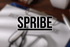 UK Gambling Commission suspends Spribe license amid hosting non-compliance and IP disputes. SPRIBE logo in bold black letters with an underline, displayed over a blurred background showing papers, eyeglasses, and a desk