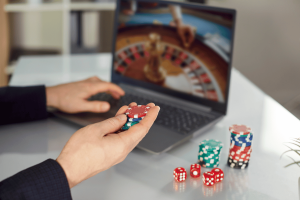 UK Gambling Commission unveils mandatory deposit limits for betting account holders. A person holding poker chips while playing an online roulette game on a laptop, representing online gambling and betting activity