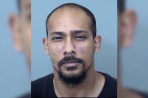 Arizona scammer gets 87 months for $5.6M fraud paying for gambling and lifestyle. Mugshot of an adult man with a shaved head and short goatee, looking directly at the camera against a plain light-blue background.