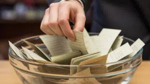 A close-up photograph of a traditional prize draw setup featuring a clear glass bowl filled with folded white paper tickets. Greater protections for players of prize draw competitions introduced