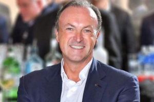 Close-up of a man wearing a suit, smiling to the camera. There are people in the background but these are blurred. Hippodrome Casino executive says talk of rise in Machine Games Duty is ‘deeply alarming’