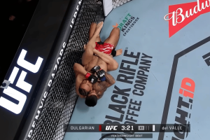 Dulgarian's 'release' fuels UFC Vegas controversy amid betting fix claims. A UFC fight scene shows one fighter on the canvas with his back against the cage while the opponent has secured back control and is attempting a choke. Both athletes wear UFC gloves and shorts as they grapple on the mat, with the Black Rifle Coffee Company logo and the fight clock visible in the octagon.