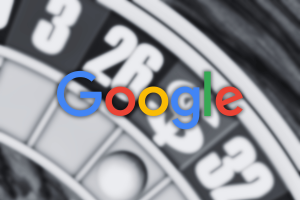 A blurred roulette wheel with numbered red, black, and green pockets appears in the background, overlaid with the multicolored Google logo in sharp focus at the center. Google takes aim at sweepstakes games, removing 'social' classification