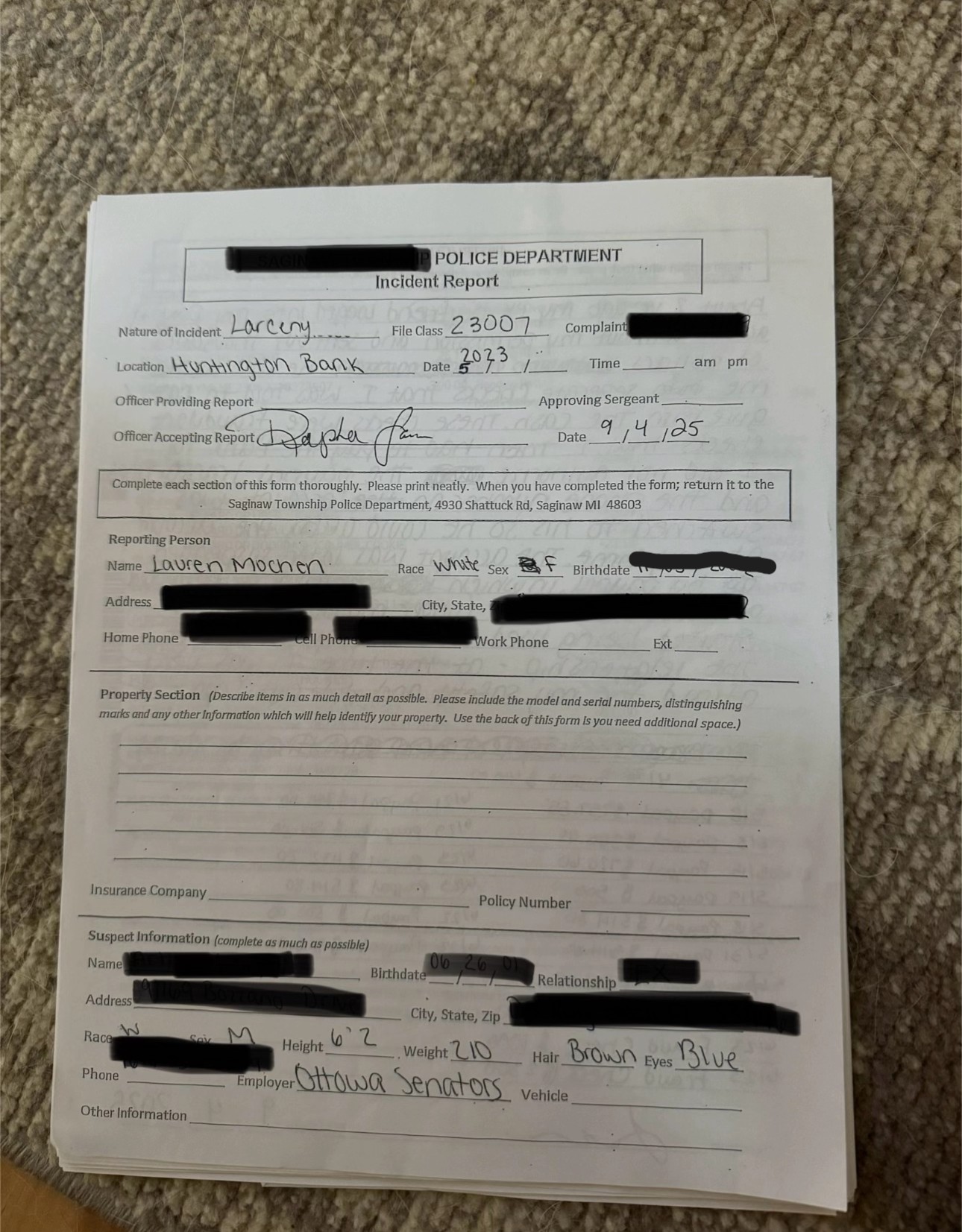 Um formulário de relatório de incidente policial colocado sobre um chão acarpetado. O relatório inclui detalhes manuscritos sobre uma denúncia de furto, com a maioria das informações pessoais ocultadas para fins de privacidade.