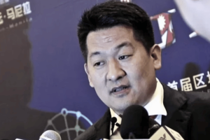 Thai court orders gambling kingpin to be extradited to China amid lengthy legal battle. She Zhijiang in a suit speaks into multiple microphones during a press event, standing in front of a blue backdrop with text and graphics.