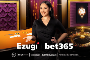 A smiling female live-casino dealer stands in front of an orange gaming table and a roulette wheel. She is wearing a black dress and gestures with one hand toward the table. The background features purple and gold decorative panels and a “25X” multiplier graphic on a screen. Logos for Ezugi and bet365 appear at the bottom, along with responsible-gambling notices. bet365 partners with Ezugi to improve live casino offerings in the UK, Ontario, and New Jersey