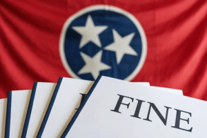 A photograph of the Tennessee state flag displayed as a backdrop with a document that says 'Fines' in the front. Tennessee Sports Wagering Council hits two 'illegal sportsbook' with fines