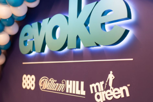 Dark background on a sign with 'evoke' sign in green and its brands listed underneath '888' 'William Hill' and 'Mr Green.' Evoke Q4 revenue hit by UK Budget