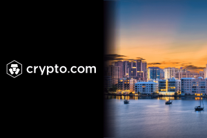 Crypto.com logo and name in white on black background beside a waterfront city skyline at sunset with lit high-rise buildings and boats on calm water. Crypto.com faces Florida lawsuit over alleged illegal sports betting
