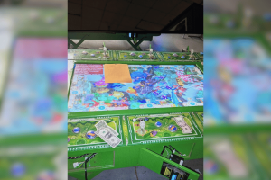Eight arrested as illegal casino is shut down by police in Pennsylvania. Close-up of an illegal casino gambling table seized during a law enforcement operation, showing a brightly colored gaming surface with underwater-themed graphics, scattered cash, poker-style chips, and small figurines, with parts of the machine open and wiring exposed, indicating it has been shut down and confiscated.