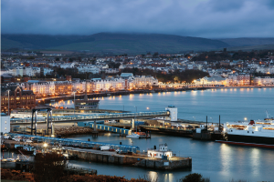 Isle of Man regulator fines gambling operator $273K for AML failures. Isle of Man cityscape at night near the harbour