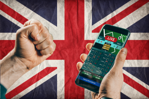 UK Gambling Commission wagering requirements chart a course for 2026. Hand holding smartphone displaying live sports betting odds against a Union Jack background, symbolising UK online gambling and regulation changes.