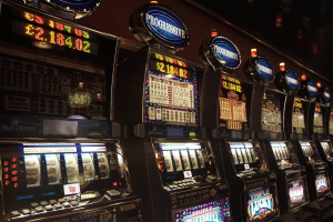 US commercial gaming revenue surges to record highs in 2025 nationwide. A row of illuminated casino slot machines with “Progressive” signs on top displays large digital jackpot amounts, including one over $2.7 million, inside a dimly lit gaming floor.