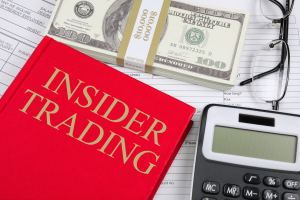 From Trading Places to war markets how insider trading slipped into prediction platforms. A red book labeled “Insider Trading” lies on paperwork beside a calculator, eyeglasses, and a stack of U.S. hundred-dollar bills.