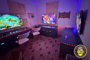 Honolulu police raid Wahiawa gambling room seize machines and cash. Room with multiple flat-screen monitors and gaming consoles set up on long tables with chairs, illuminated by colorful LED lights, inside an alleged illegal gambling operation raided by the Honolulu Police Department in Wahiawā.