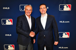 MLB Commissioner Rob Manfred and CFTC chairman Mike Selig shake hands at Major League Baseball partnership announcement event with MLB logos backdrop
